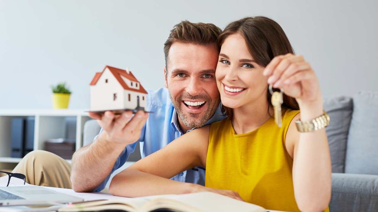 two people holding up a house figurine and keys